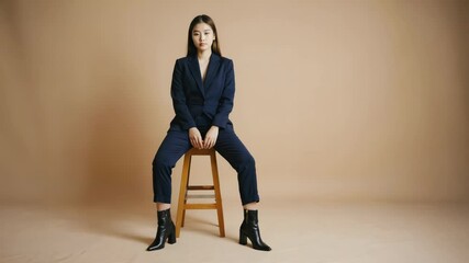 Aufkleber - A woman sits on a stool, dressed in suit and boots, ready for action.