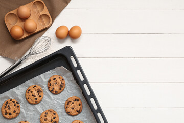 Wall Mural - baking tray of sweet cookies with chocolate chips and eggs on white wooden background