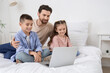 © Pixel-Shot - Happy father with his little children watching cartoons on laptop in bedroom