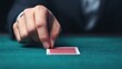 © Tanakrit - A hand delicately touches a playing card on a green felt surface, suggesting a moment of concentration or strategy in a card game.