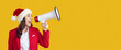 © Studio Romantic - Santa Claus announcement. Positive woman screaming in megaphone saying dont miss Christmas or New Year sales, dressed in red costume, isolated over yellow background with blank space on right side