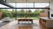 © Ninja in Pajamas - A large open living room with a wooden table and chairs, a potted plant, and a kitchen. The room has a modern and spacious feel, with a lot of natural light coming in from the large windows