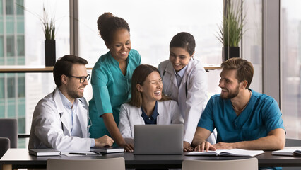 Celebrate professional success. Diverse young doctors medical workers team feel happy look on notebook screen laugh succeeding in research project get positive feedback from patient on clinic website