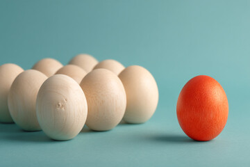 Poster - Group of beige wooden eggs and single orange egg on teal background, showcasing uniqueness and standing out from the crowd