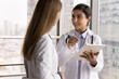 © fizkes - Problem solving together. Young woman doctor medical worker talk to female colleague pharmacist physician discuss healthcare research article on tablet computer screen ask opinion professional advice