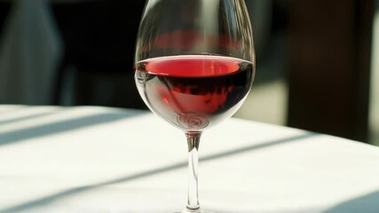 Poster - A single glass of red wine sits on a wooden table, ready for consumption.