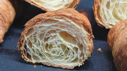 Poster - A piece of croissant is cut in half. The other half is not visible. The croissant is on a black surface