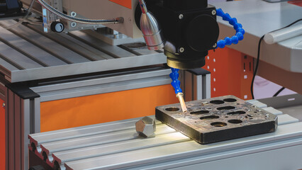 Aufkleber - A machine is working on a piece of metal. The machine is orange and silver. The machine is making a hole in the metal