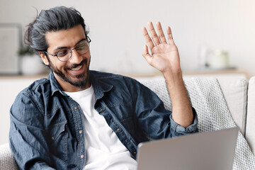 Poster - Joyful Young Arab Guy Having Online Video Call On Laptop At Home, Waving Hand At Camera, Talking With Family While Relaxing On Couch In Living Room, Enjoying Online Communication, Copy Space