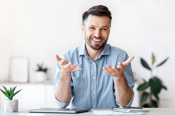 Poster - Successful handsome businessman sitting at desk in office, talking at camera, sharing his experience and ideas, free space
