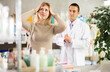 © JackF - Woman came to a European pharmacy with a headache in search of medicine. Buyer looking for migraine pills against the background of a pharmacist