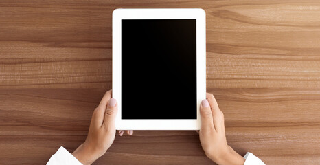Aufkleber - Mock up image of two hands holding digital tablet with isolated black screen, wooden table in the background