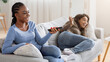 © Prostock-studio - Two cute black ladies having fun on weekend at home, watching TV on sofa at living room, empty space. Happy african american women friends laying on couch, watching funny content on television