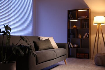 Poster - stylish living room with comfortable sofa and wooden shelving unit in evening. interior design