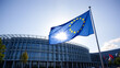 © Zachary - Flag of European Union waving in the wind in front of the modern parliament building on sunny day. Happy Europe day. European Parliament elections. European dream. Future of Europe