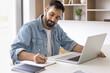 © fizkes - Remote work lifestyle. Confident millennial businessman entrepreneur freelancer engaged in business planning take brief notes write down information ideas from notebook screen sitting at office desk