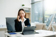 © Nuttapong punna - Young Asian businesswoman smiling and working with tablet and laptop in office.