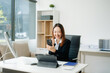 © Nuttapong punna - Young Asian businesswoman smiling and working with tablet and laptop in office.