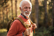 © Jelena - Senior Man Smiling While Adventuring Through Forest with Backpack On