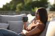 © PheelingsMedia - Woman relaxing drinking coffee sitting in exterior sofa in a terrace
