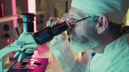 Wall Mural - experienced researcher wearing lab coat and glasses carefully adjusting microscope while conducting 