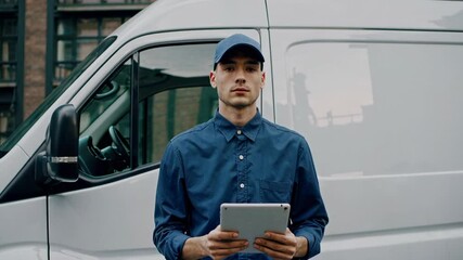 Poster - Serious delivery man in uniform and cap uses tablet next to white van, checking shipping information, managing logistics, and ensuring efficient delivery in urban area