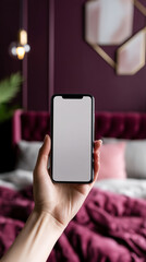 Aufkleber - Hand holding smartphone with blank screen against blurred background of burgundy bedding and decor, showcasing mockup for app or website display