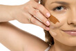 © vladimirfloyd - Extreme close-up of woman's face with hand displaying three foundation shades swatched on cheek, showing makeup color testing detail against white background