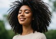 © Ozz - A serene black woman with curly hair smiles, feeling calm and content with eyes closed.