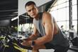 © Davidovici - Serious concentrated fit guy in sportswear exercising on stationary bike at gym fitness. Athlete male training on exercise bike and looking aside. Young man working out at a class in the modern gym.