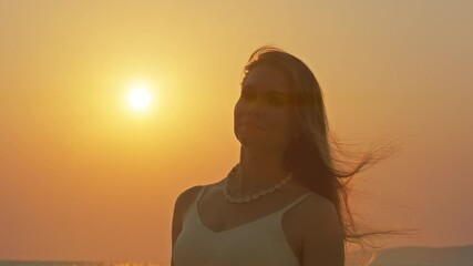 Wall Mural - young woman with long hair enjoying sunset at beach with golden reflections on sea water