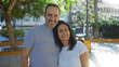 © Krakenimages.com - Middle age hispanic couple smiling together in an urban park setting, expressing love and family bonds amid city streets and outdoor greenery.