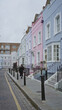 © Krakenimages.com - Woman walking down chelsea street in london with colorful houses lining the path under a cloudy sky.