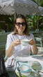 © Krakenimages.com - Woman enjoying coffee on a luxury restaurant terrace, wearing sunglasses and a white outfit, surrounded by stylish decor and natural greenery under sunlight.
