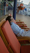 © Krakenimages.com - Woman relaxing on cruise ship deck with ocean view, enjoying leisure time outdoors on sunny day, dressed in casual outfit, surrounded by lifeboats and dock scenery.