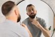© New Africa - Man trimming beard with scissors near mirror in bathroom