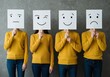 © Selda - Four people showcase different emotions by holding up cards with facial expressions on a gray background.