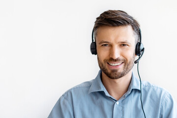 Poster - Portrait of smiling male customer service operator in headset posing at workplace, looking at camera, portrait of handsome hotline manager sitting at desk with laptop in white office, copy space