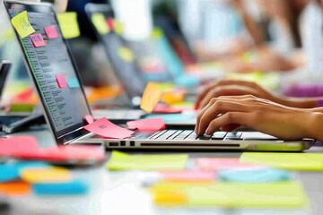 Leinwandbilder - Busy workspace filled with colorful sticky notes and focused individuals typing on laptops during a collaborative project session