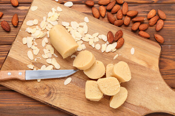 Wall Mural - cutting board with tasty marzipan, knife, almond nuts and flakes on wooden background, closeup