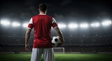Back view of a soccer player standing on a soccer field holding a ball in a stadium at night