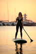 © zhagunov_a - Woman Paddleboarding at Sunset in Marina Harbor