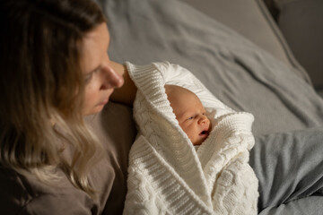 Aufkleber - Mom cuddles newborn baby wrapped in cozy blanket during quiet evening at home, expressing love and connection in a serene atmosphere
