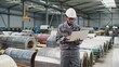 © VAKSMANV - Serious African American engineer using laptop at workplace. Worker wearing helmet and uniform standing in large storage. Inspector of manufacture working with technology device at warehouse.