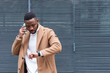 © BUDDHA - African American man checking time while making phone call close up, confident positive businessman planning meeting with partner, looking at wristwatch, task management