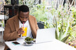 © BUDDHA - Man sits at cafe table, working on laptop and drinking healthy juice