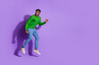© deagreez - Young fashionable man in vibrant casual attire jumping playfully against a bold purple background, exuding energy and modern style.