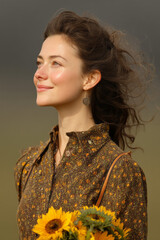 Poster - Woman holding bunch of sunflowers in field with wind in hair. 