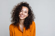 © Bohdan - Smiling woman with curly hair in an orange shirt on a plain light background, conveying happiness and positivity, ideal for lifestyle and fashion themes