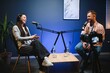 © Serhii - Female podcaster in headphones interviewing man guest using microphone, smiling, recording and broadcasting audio podcast in studio. Content creator, blogging